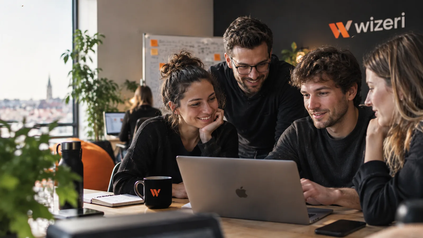 Four colleagues around one laptop in the Cluj office, afternoon light from the window